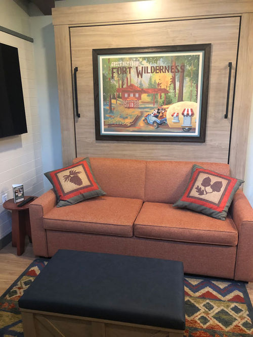 The living and dining area features a sofa in front of a Murphy-style queen bed hidden in the wall.